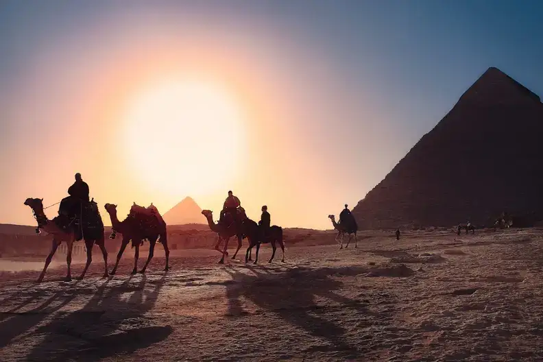Five people riding camels across the sand beside a pyramid in Egypt